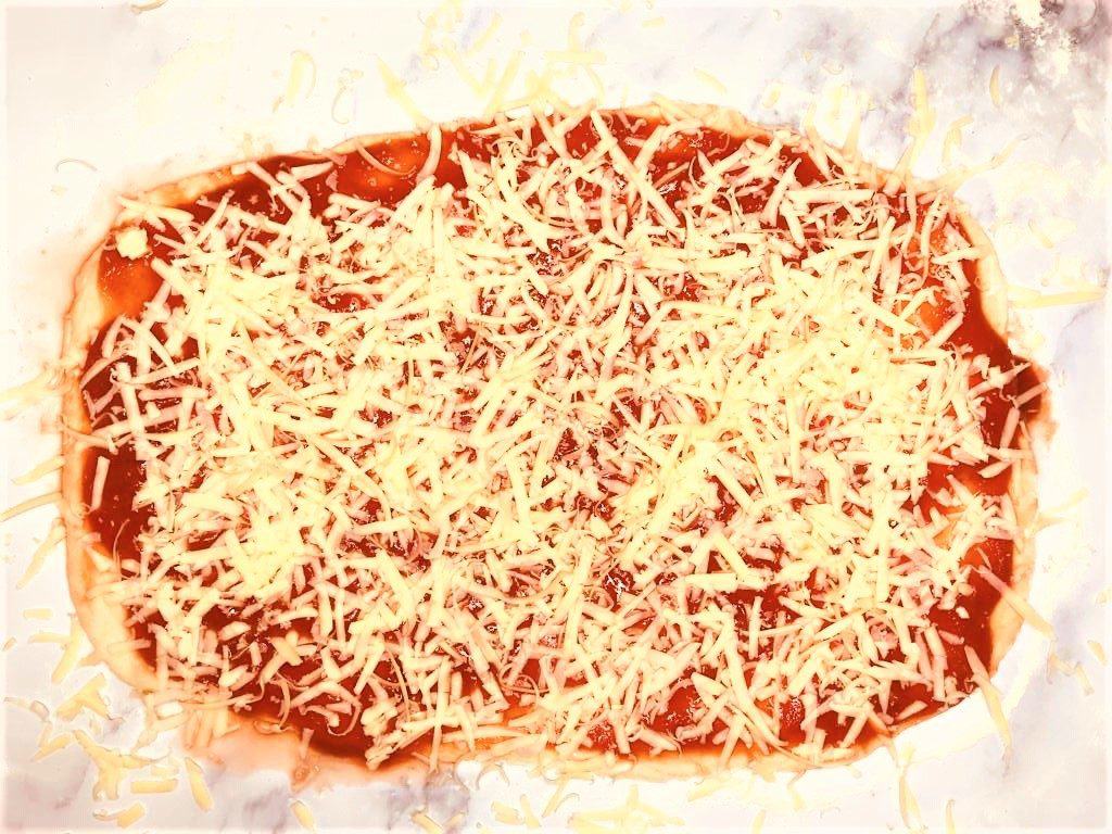 rolled out pizza dough with sauce and cheese on top