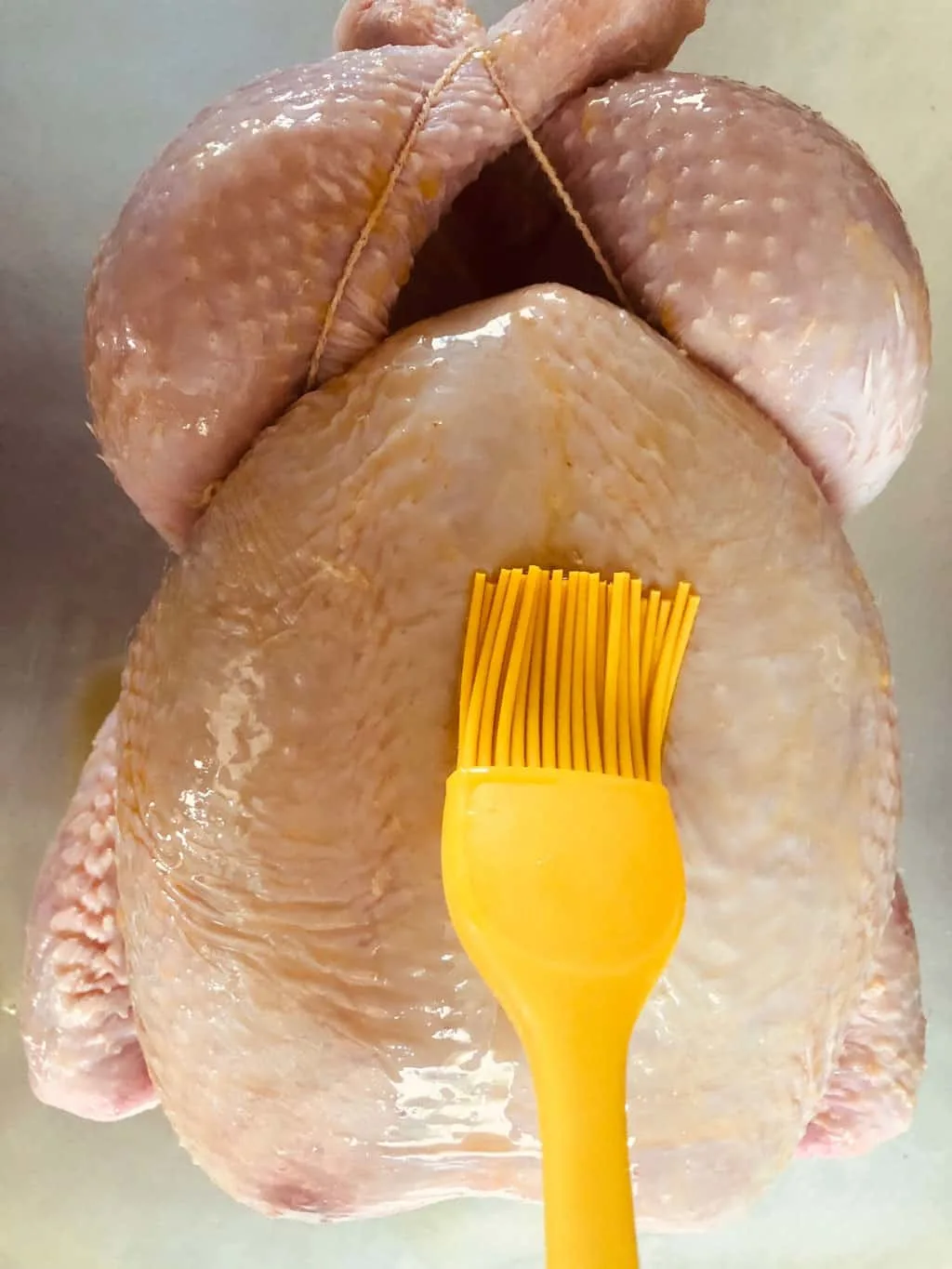 yellow silicone brush basting oil on a raw whole chicken