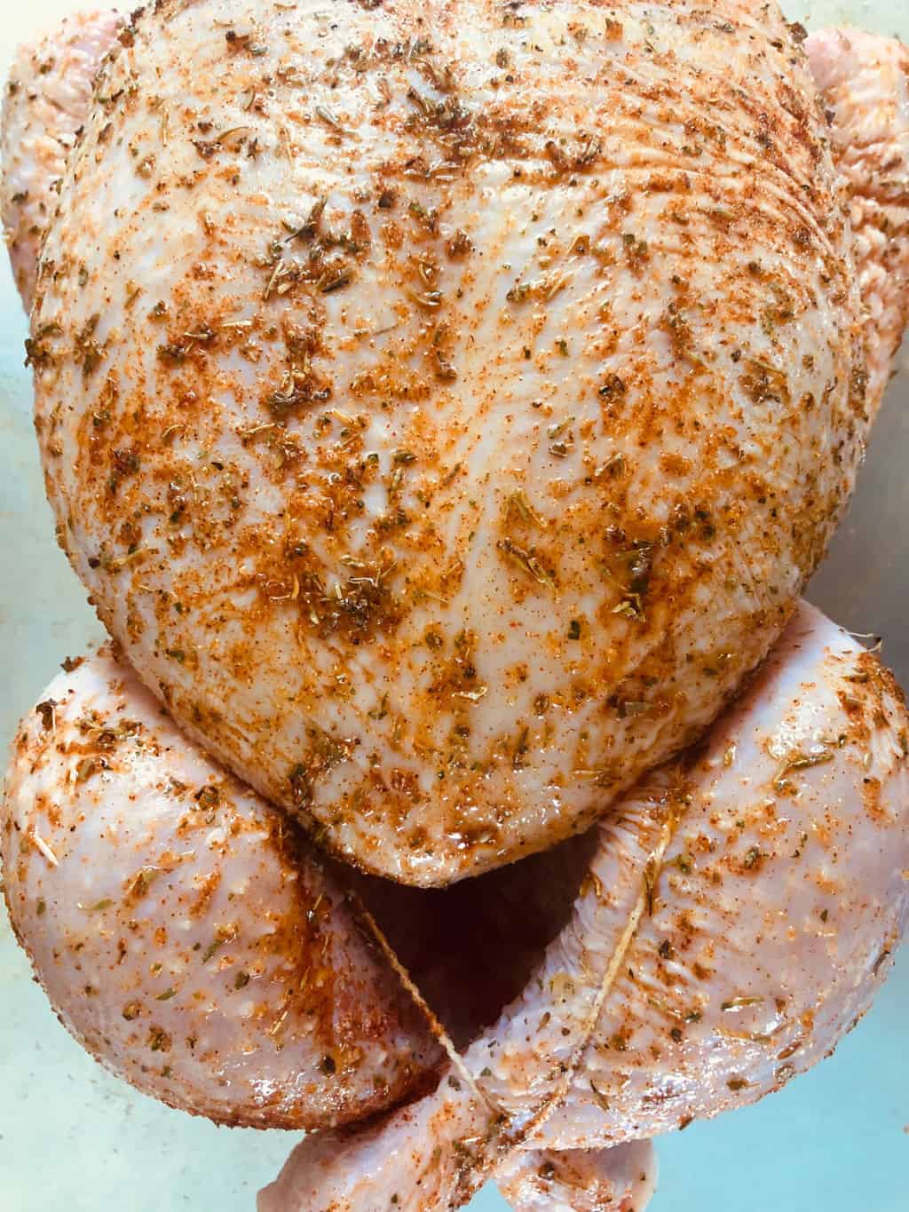 herbs and spices basted over breast of whole raw chicken