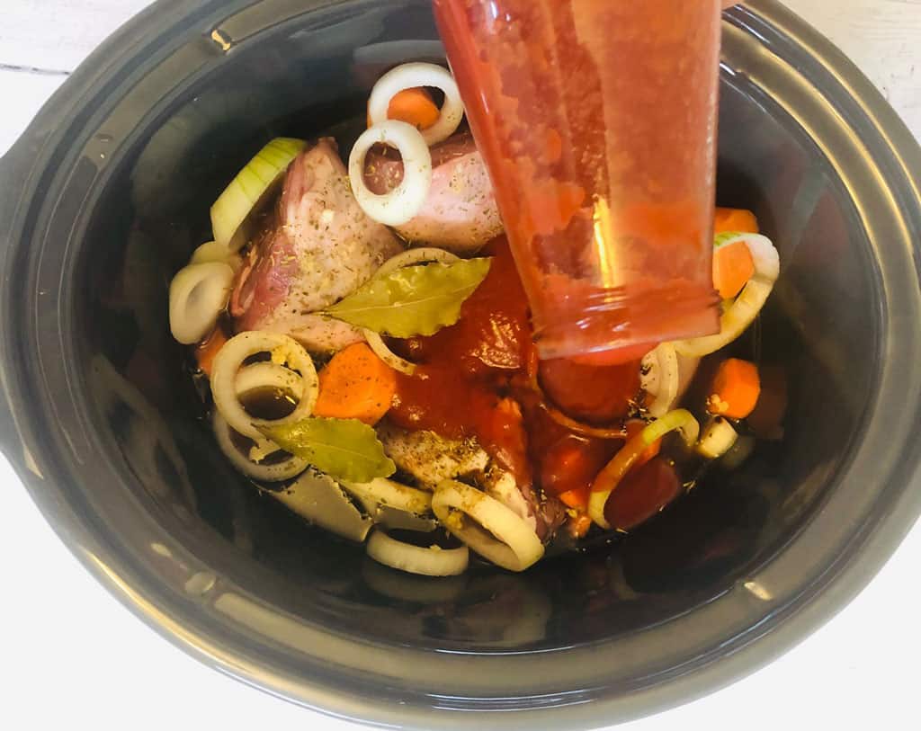 pouring passata over lamb shanks ingredients in slow cooker