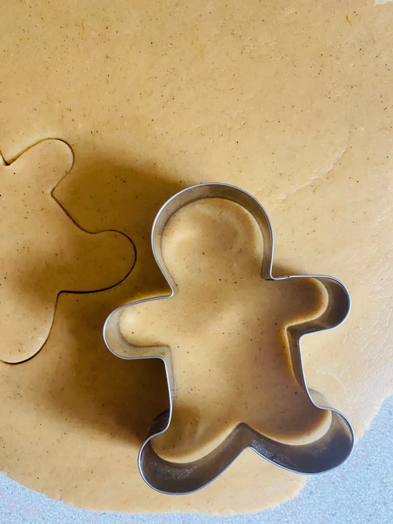 using a gingerbread man cutter to cut out cookie shapes from dough