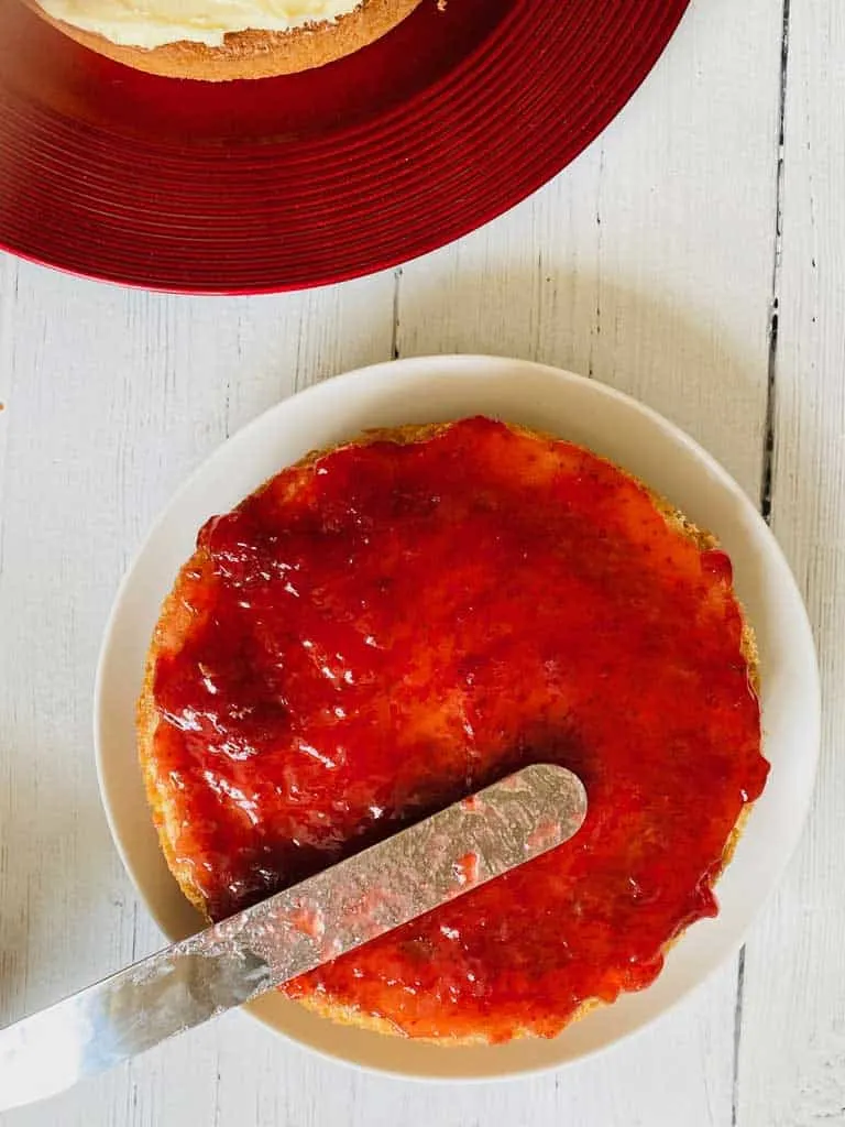 spreading jam on victoria sponge cake