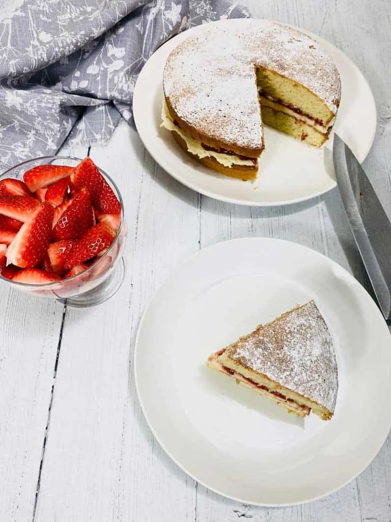 victoria sponge cake slice with cake in the background and sliced strawberries