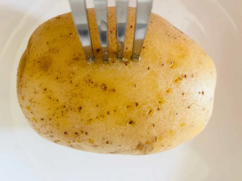 fork piercing baked potato before cooking in microwave