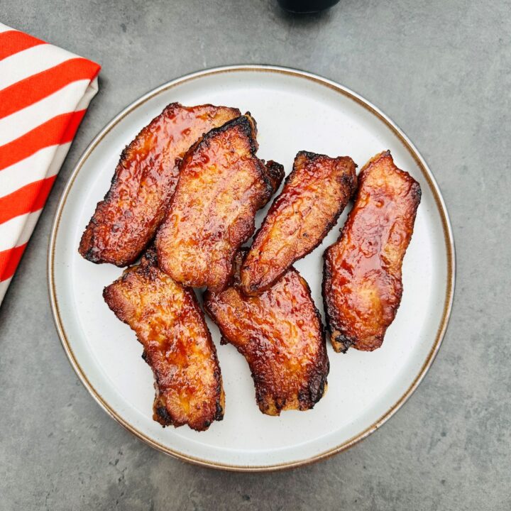 BBQ pork belly slices on a plate next to a red and white striped tea towel and an air fryer