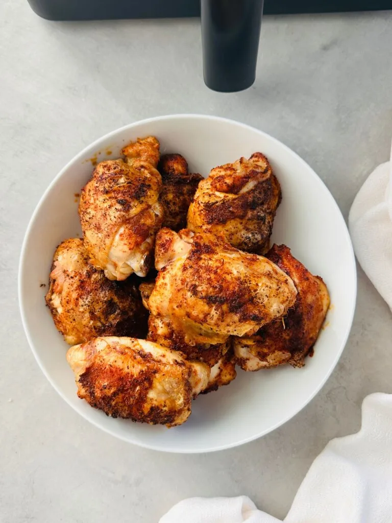 cooked chicken thighs on a white plate with part of an air fryer showing