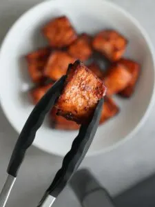 air fryer salmon bite held in some silicone tongs above a bowl of more salmon bites