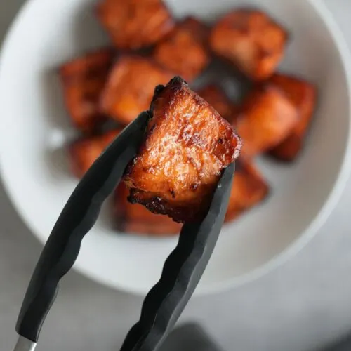 air fryer salmon bite held in some silicone tongs above a bowl of more salmon bites