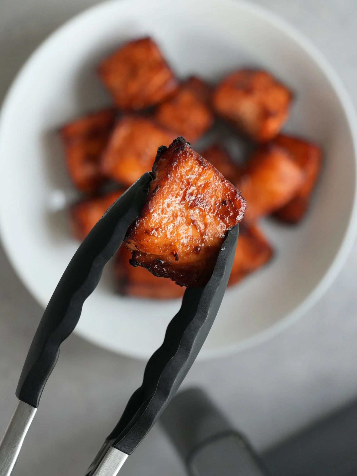 air fryer salmon bite held in some silicone tongs above a bowl of more salmon bites