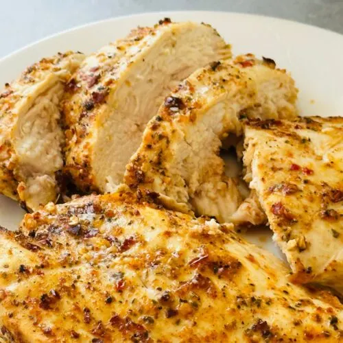 sliced piri piri chicken breast on a white plate next to an air fryer