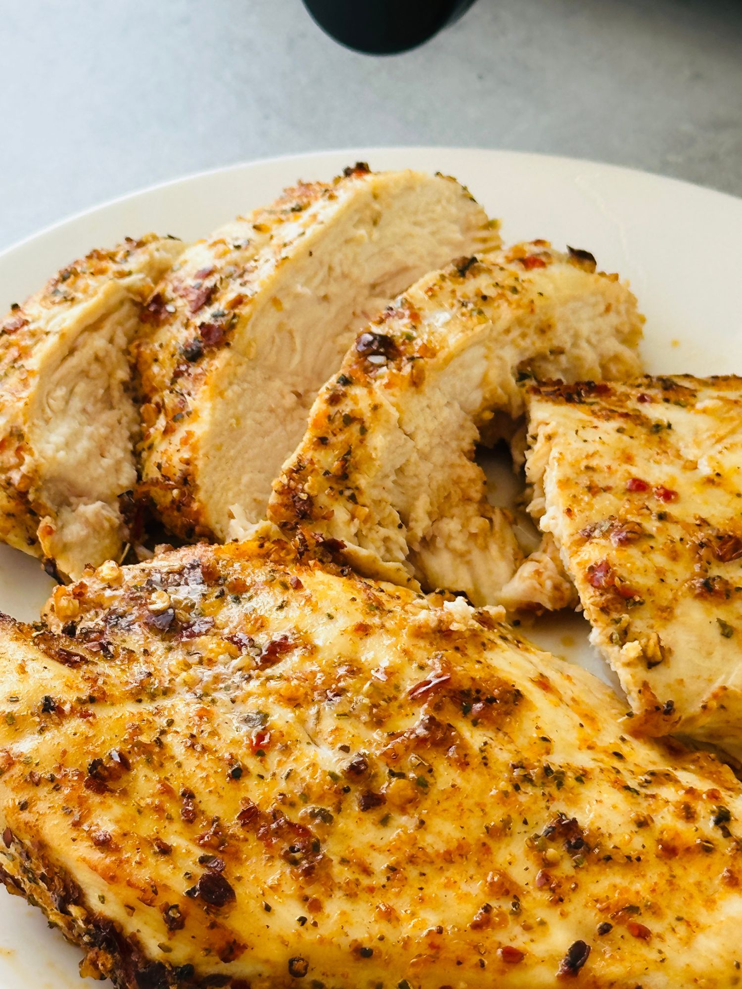 sliced piri piri chicken breast on a white plate next to an air fryer