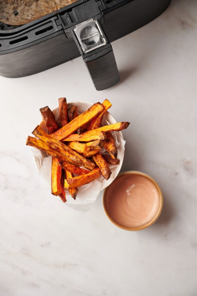 sweet potato fries next to some sauce and an air fryer