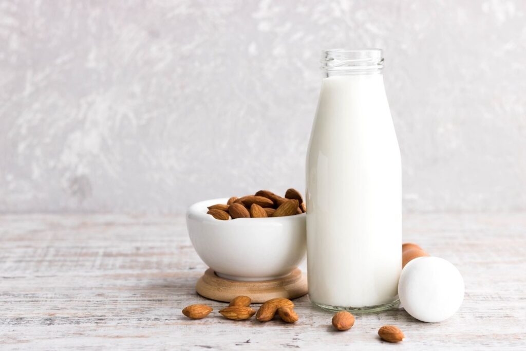 Almond milk in a bottle next to a bowl of raw almonds