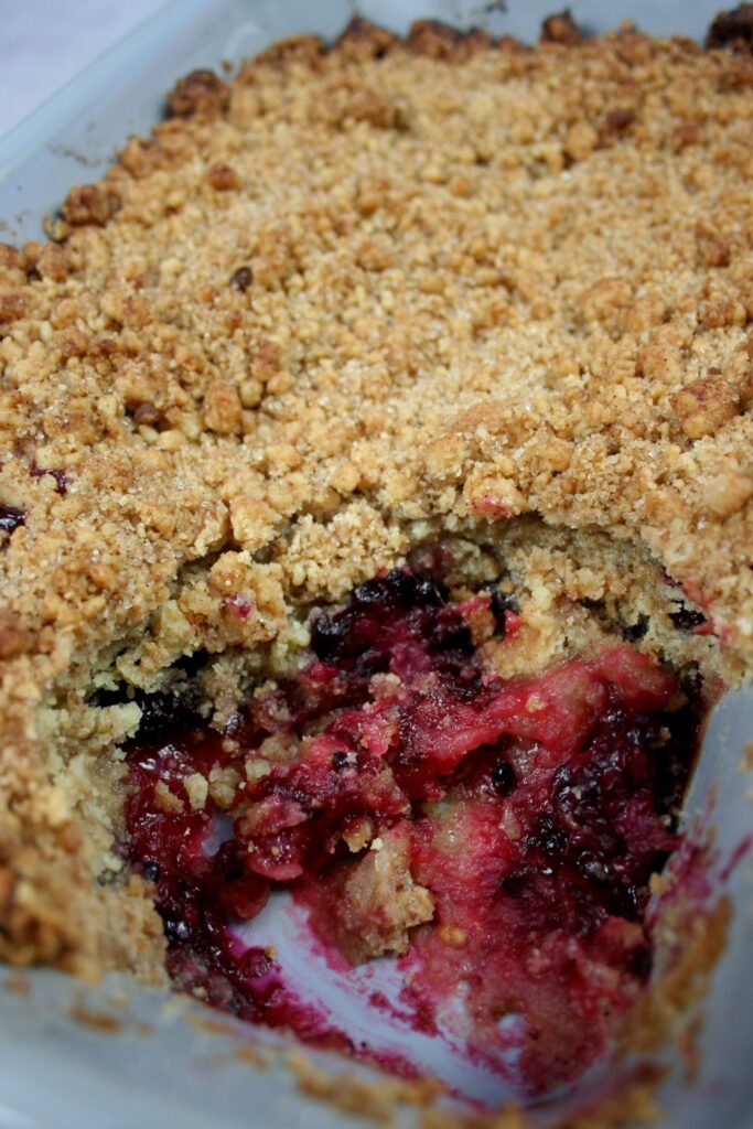 apple and blackberry crumble in an oven dish with one portion removed