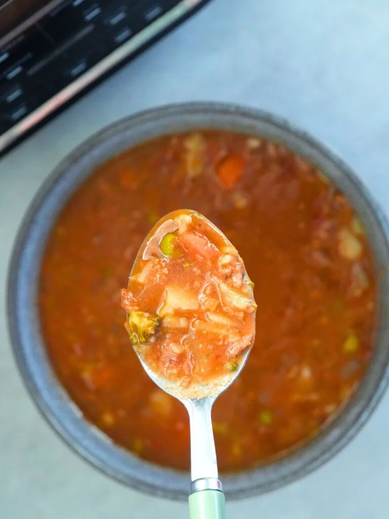 beef and vegetable soup on a spoon over a bowl in front of a Ninja Soup Maker