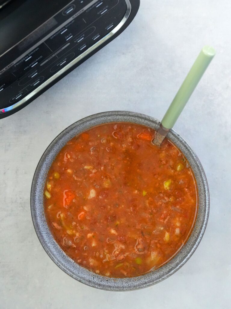 beef and vegetable soup in a bowl in front of a soup maker