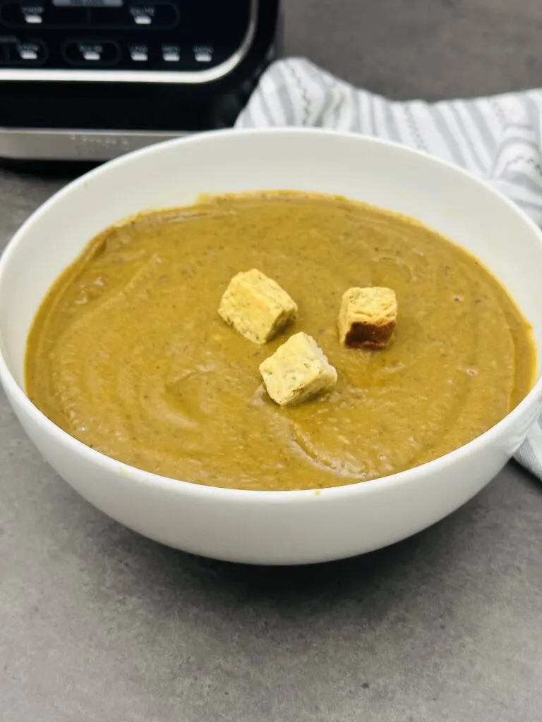 black bean and sweet potato soup with croutons in a bowl next to Ninja soup maker