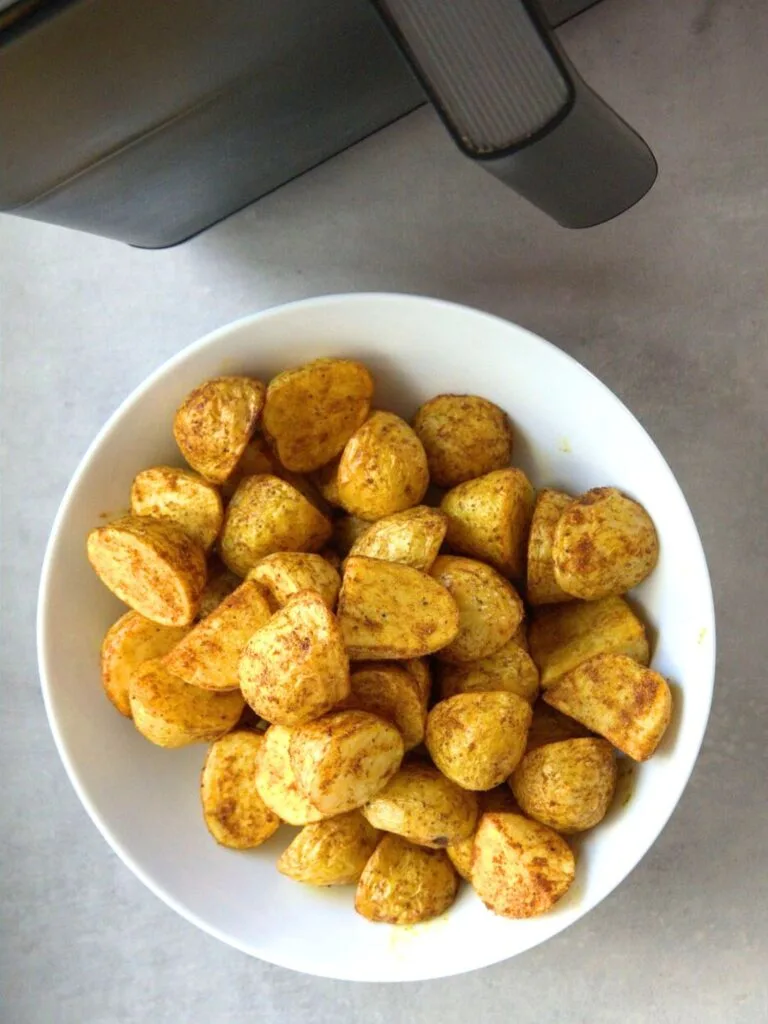 cooked Bombay style new potatoes in a white bowl next to an air fryer