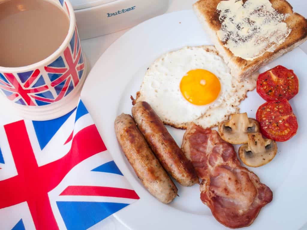 Full English breakfast next to a Union Jack flag and cup of tea in a Union Jack mug