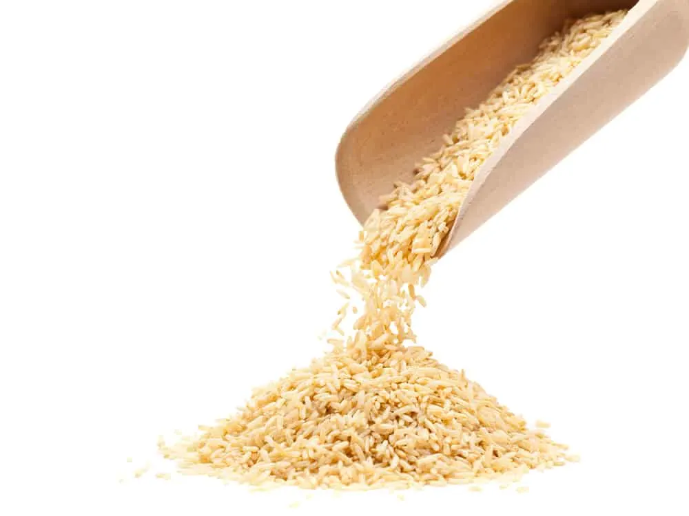 Raw organic brown rice poured from wooden scoop over white background