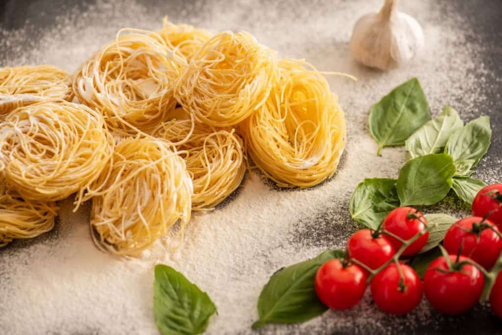 Capellini pasta next to garlic and tomatoes