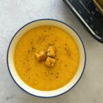 carrot and parsnip soup in a bowl with croutons and black pepper seasoning next to a Ninja soup maker