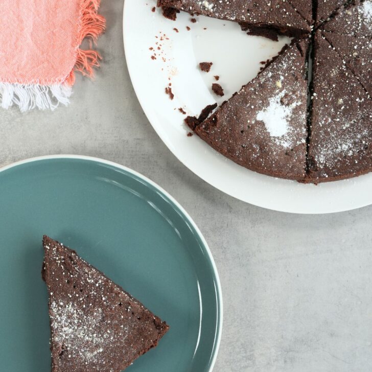 slice of chocolate shortbread on a plate next to a larger plate with the remaining chocolate shortbread pieces with a pink tea towel on the side