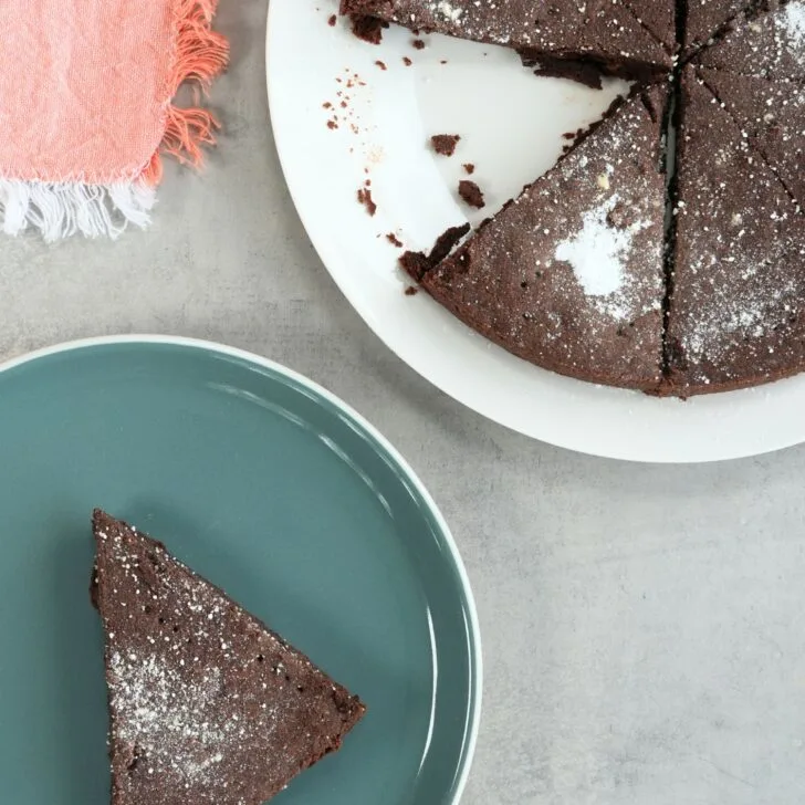 slice of chocolate shortbread on a plate next to a larger plate with the remaining chocolate shortbread pieces with a pink tea towel on the side