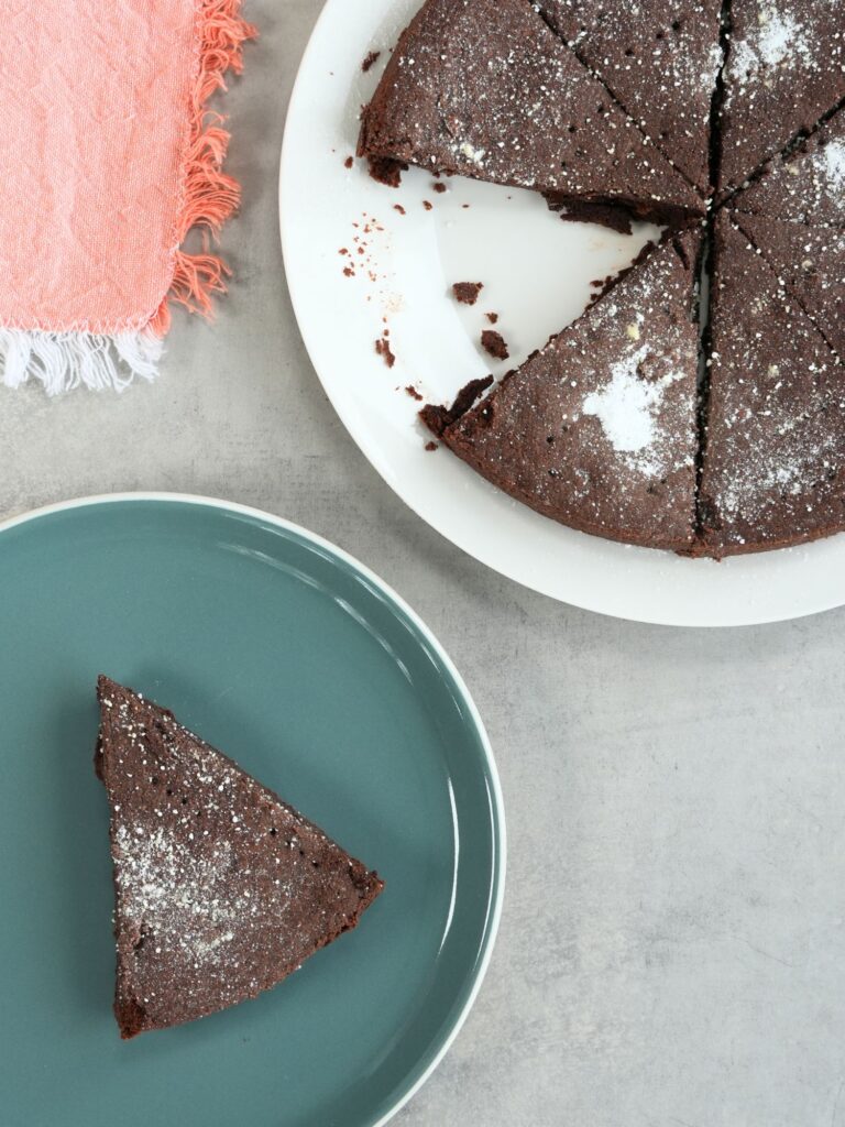 slice of chocolate shortbread on a plate next to a larger plate with the remaining chocolate shortbread pieces with a pink tea towel on the side 