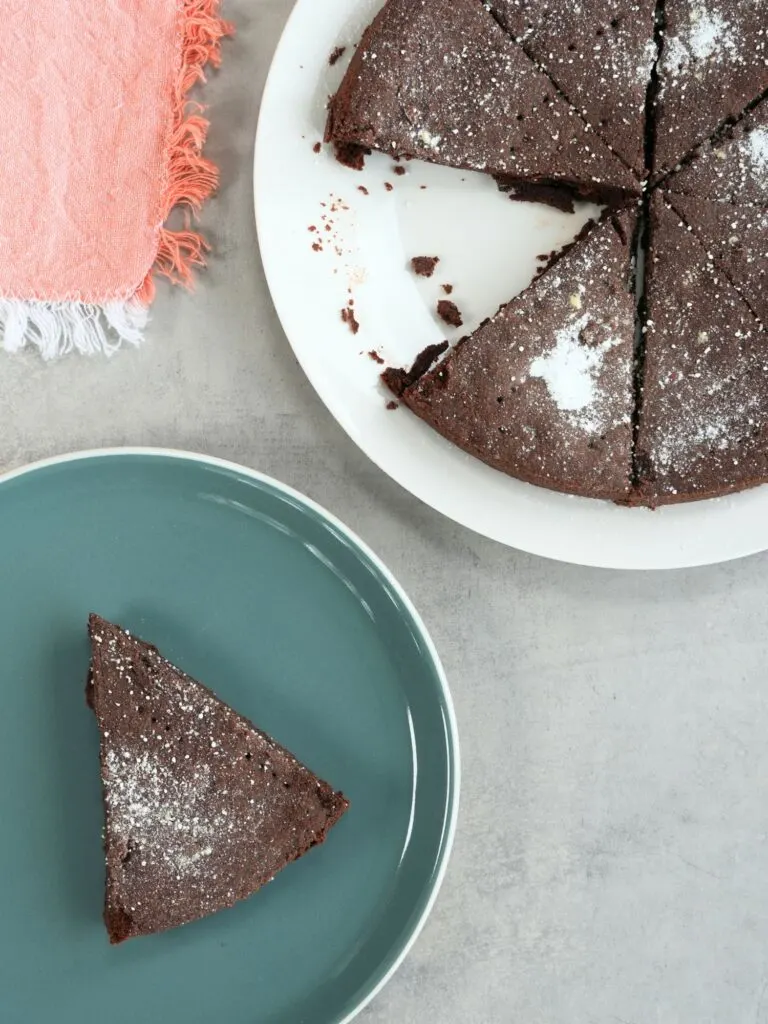 slice of chocolate shortbread on a plate next to a larger plate with the remaining chocolate shortbread pieces with a pink tea towel on the side