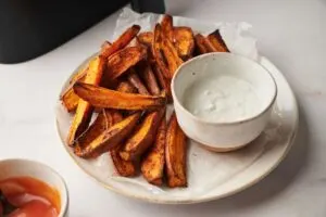sweet potato wedges on a plate next to a dip and air fryer