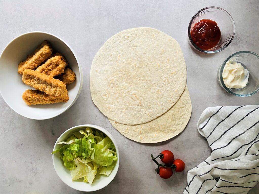 ingredients for making fish finger wraps - fish fingers, tortilla wraps, lettuce, tomatoes, tomato ketchup and mayonnaise
