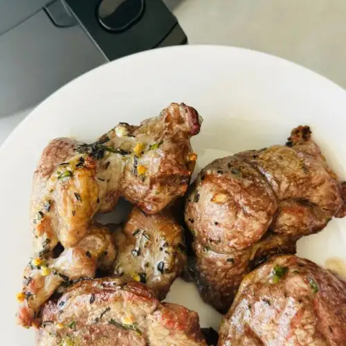 cooked lamb steaks with garlic and rosemary on a plate next to an air fryer