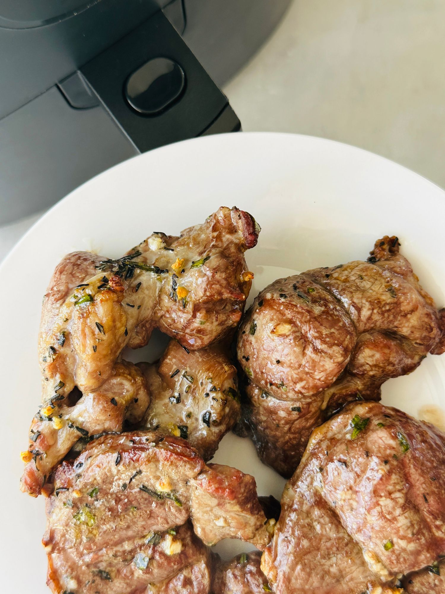 cooked lamb steaks with garlic and rosemary on a plate next to an air fryer