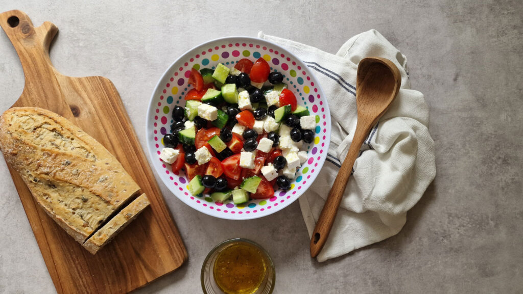 Greek salad in a bowl next to sourdough bread on a chopping board