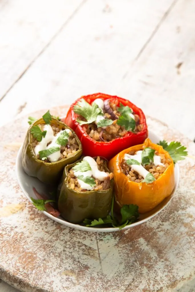 4 slow cooker stuffed peppers served on a plate with sour cream and fresh coriander on top.