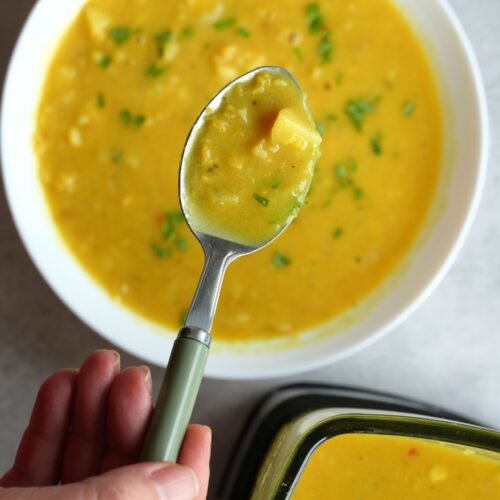 Lentil, Potato and Coconut Soup on a spoon with bowl of soup below it and part of a soup maker jug in the corner