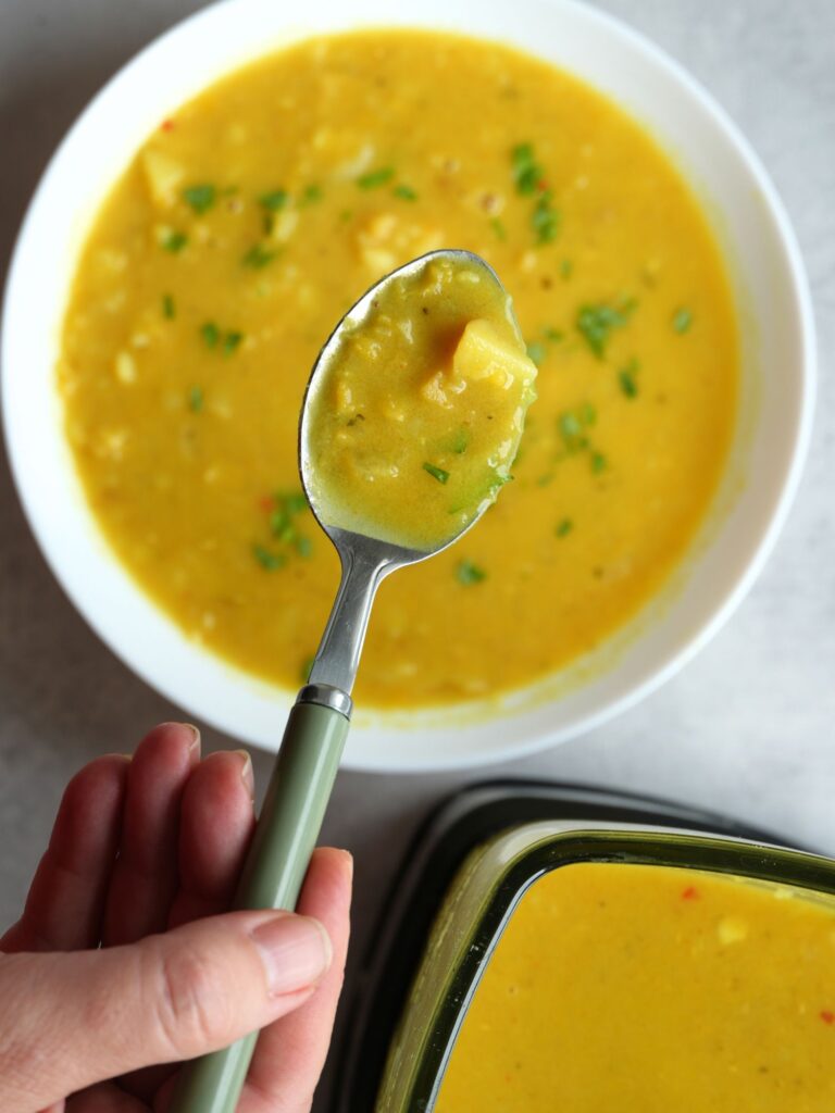 Lentil, Potato and Coconut Soup on a spoon with bowl of soup below it and part of a soup maker jug in the corner