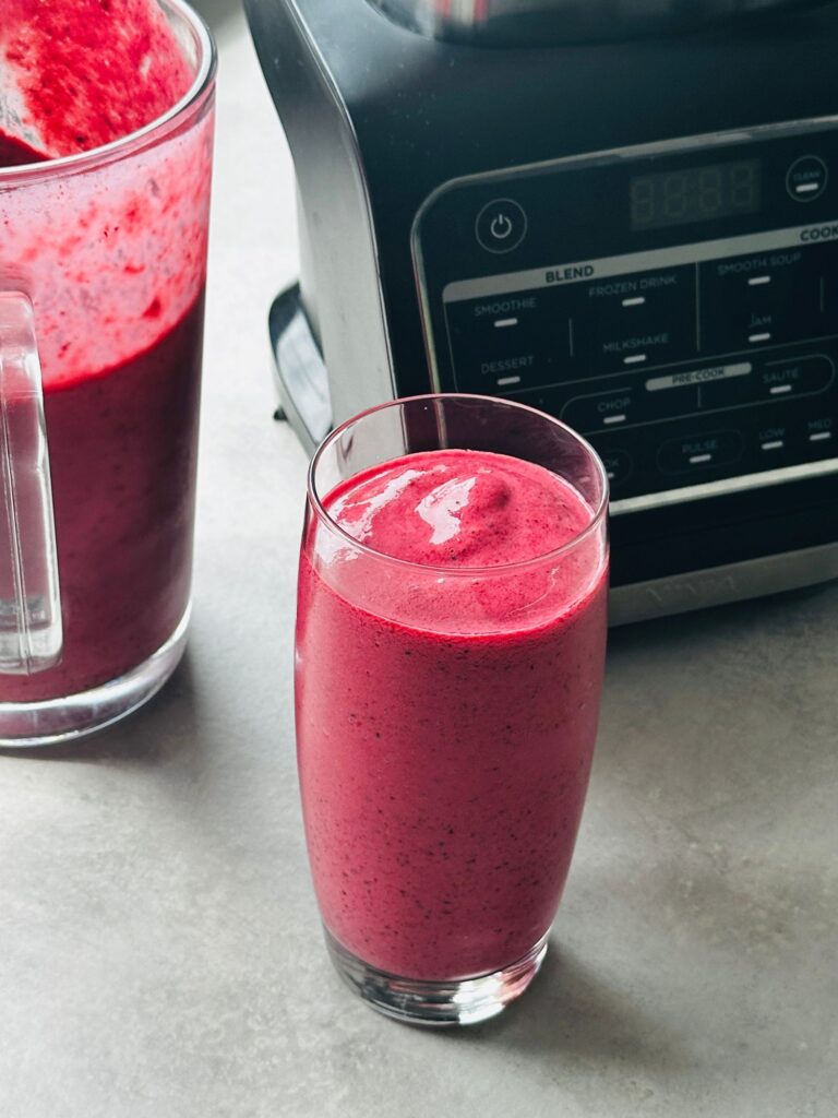 mixed berry smoothie poured into a glass in front of the Ninja hot and cold blender and next to a jug with some of the smoothie in it