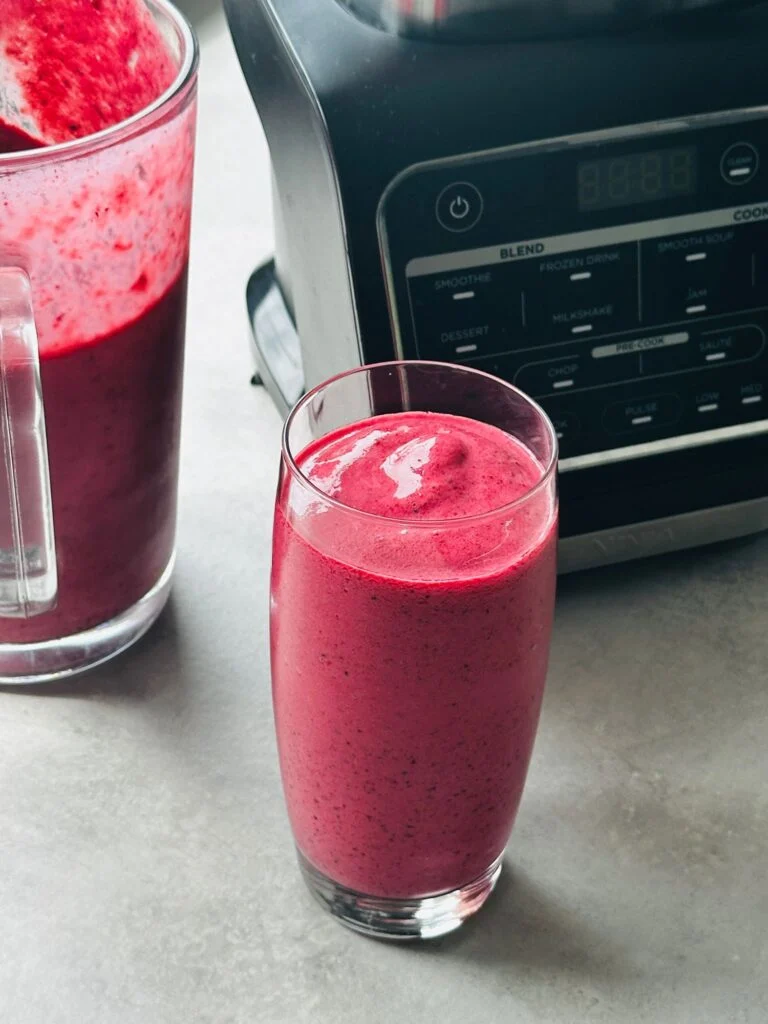 mixed berry smoothie poured into a glass in front of the Ninja hot and cold blender and next to a jug with some of the smoothie in it