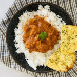 Chicken curry on a plate with white rice and naan bread