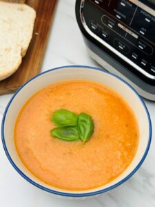 tomato and basil soup in a bowl next to a Ninja soup maker