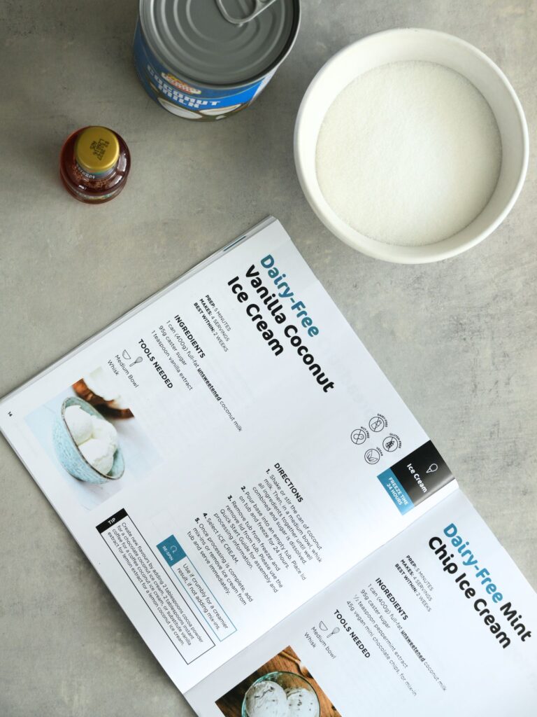 Ninja creami recipe book open on recipe next to sugar and coconut milk and vanilla extra
