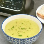 Leek and potato soup in a bowl next to a Ninja soup maker with a plate and slice of white bread