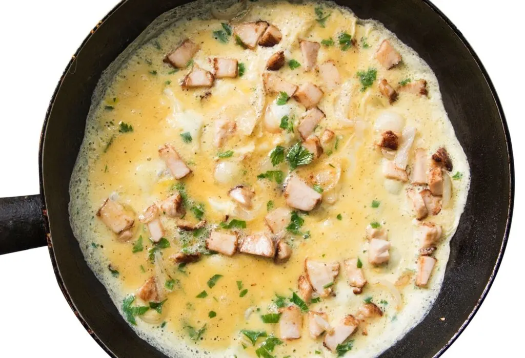 cooking omelette in a pan with herbs and mushrooms