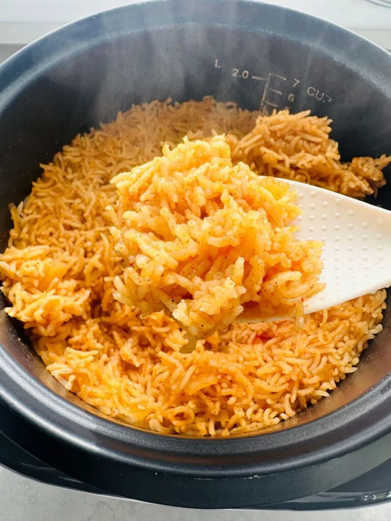 cooked Mexican style rice in a rice cooker with a white spoon holding some up with steam coming off