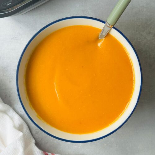 roasted tomato and garlic soup in a bowl with a spoon in it next to a white teatowel and a ninja soup maker