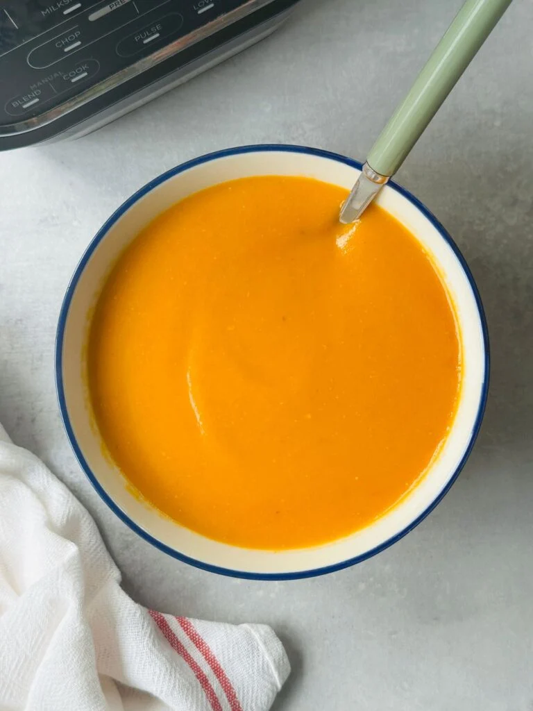 roasted tomato and garlic soup in a bowl with a spoon in it next to a white teatowel and a ninja soup maker