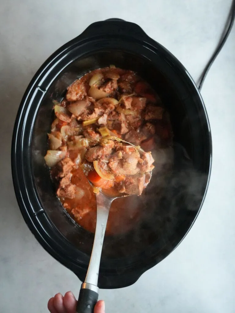 cooked pork casserole in slow cooker, serving spoon holding some up above the slow cooker pot