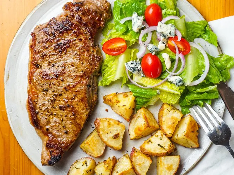 pan fried steak on a plate with a side of roasted potatoes and salad 